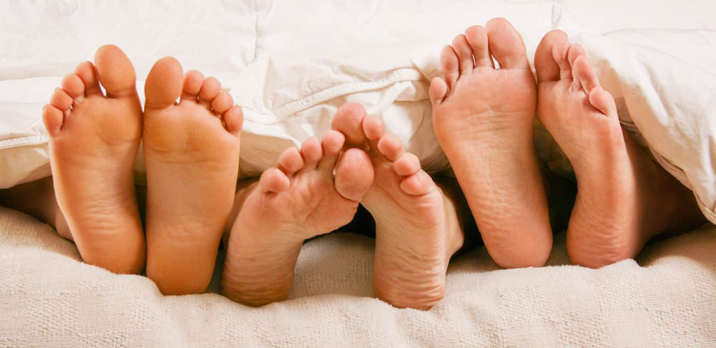 A family of feet being shown from under a blanket.