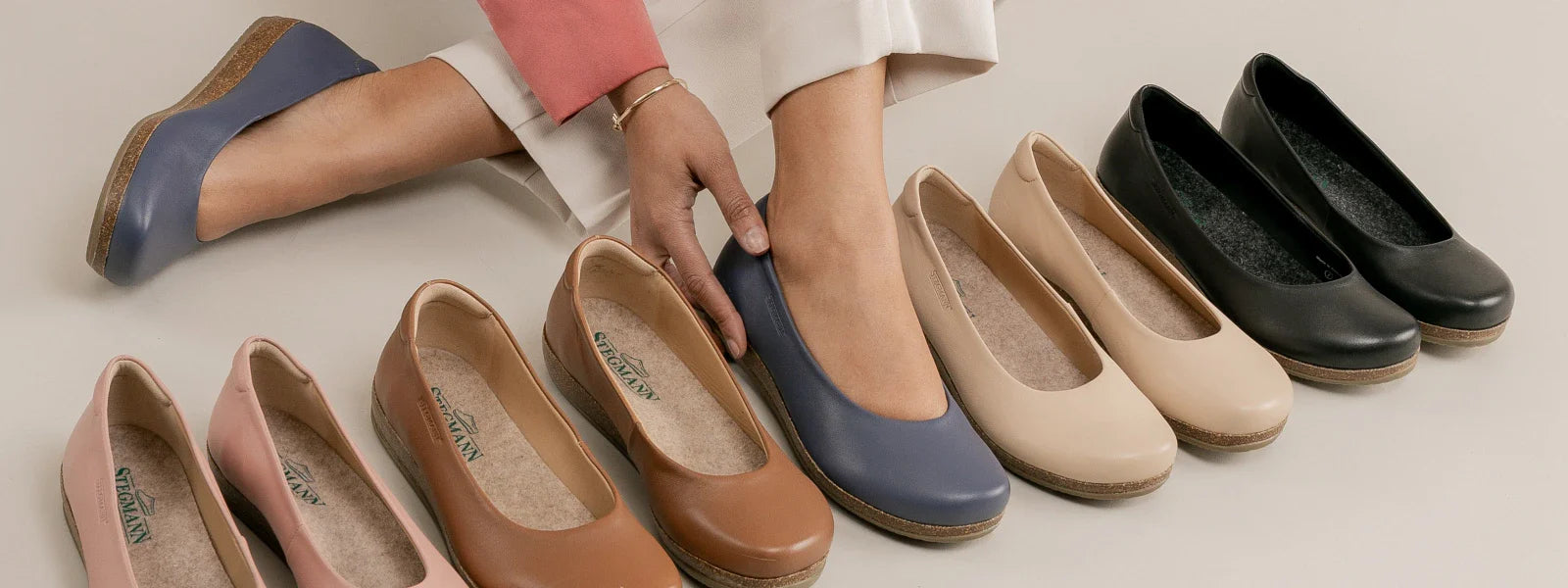 A person tries on a blue ballet flat from a row of women's flats in various colors including pink, tan, brown, blue, beige, and black.