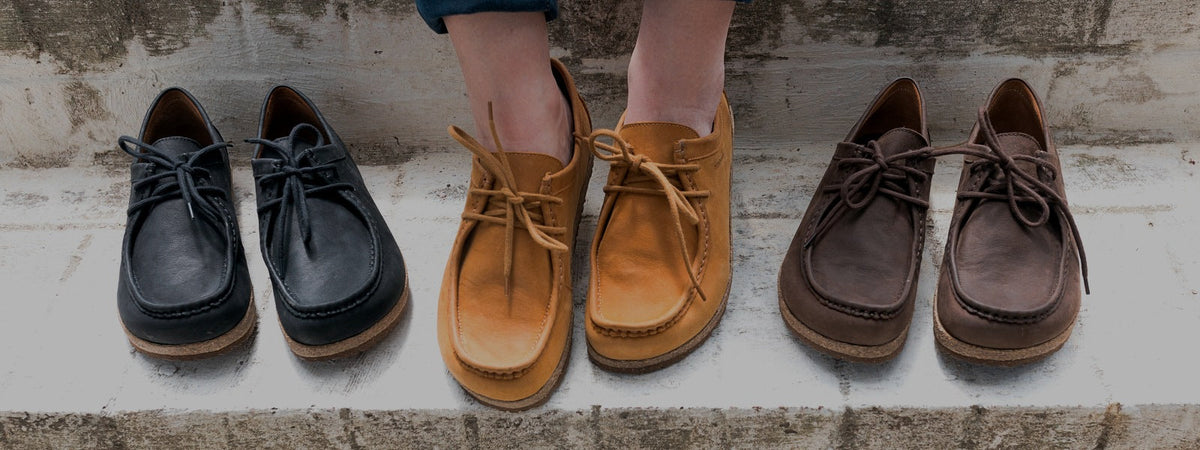 A person tries on a blue ballet flat from a row of women's flats in various colors including pink, tan, brown, blue, beige, and black.