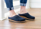 Someone wearing the Women's Original 108 Wool Clog - Wide, crafted from Merino wool felt with supportive cork soles, stands on a wooden floor.