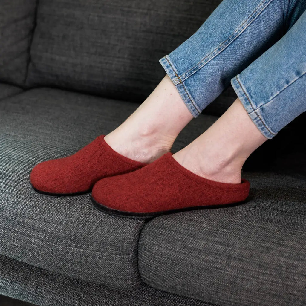 A person wearing Women's Alpine Comfort Wool Slippers and blue jeans sits on a dark gray couch.