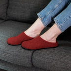 A person wearing Women's Alpine Comfort Wool Slippers and blue jeans sits on a dark gray couch.