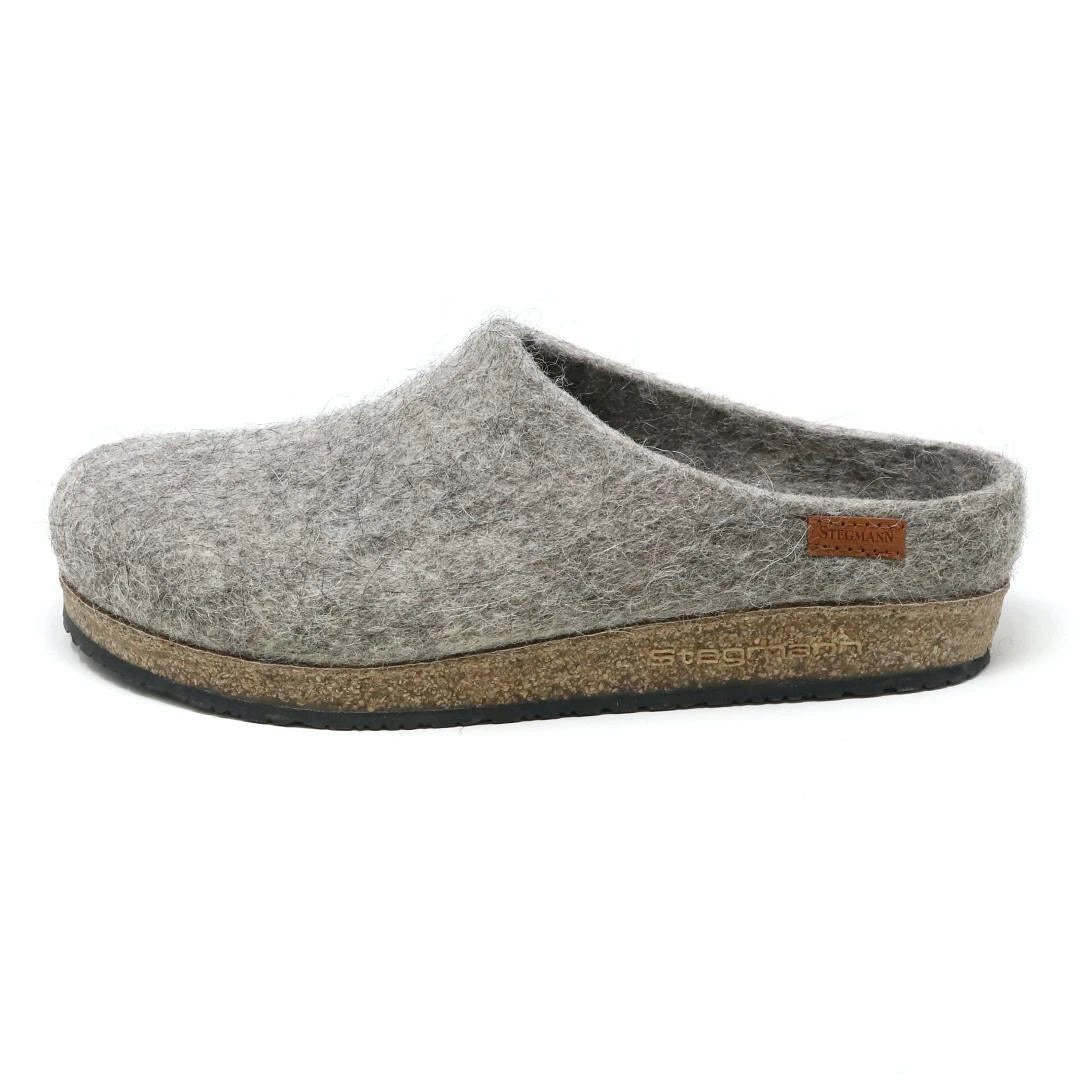 The Women's Eco Wool Clog is shown in grey felt with a cork latex footbed and small brown stitched side tag, viewed from the left. This sustainable wool footwear blends comfort and eco-friendly design.