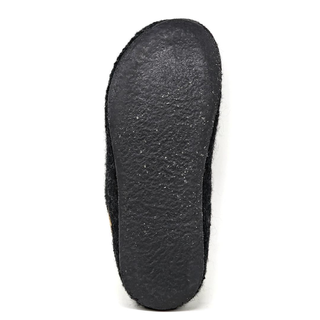 The image depicts the underside of a Men's Alpine Comfort Wool Slipper in black, featuring a subtly textured sole. The design suggests an anatomically shaped cork insole for enhanced comfort and support.