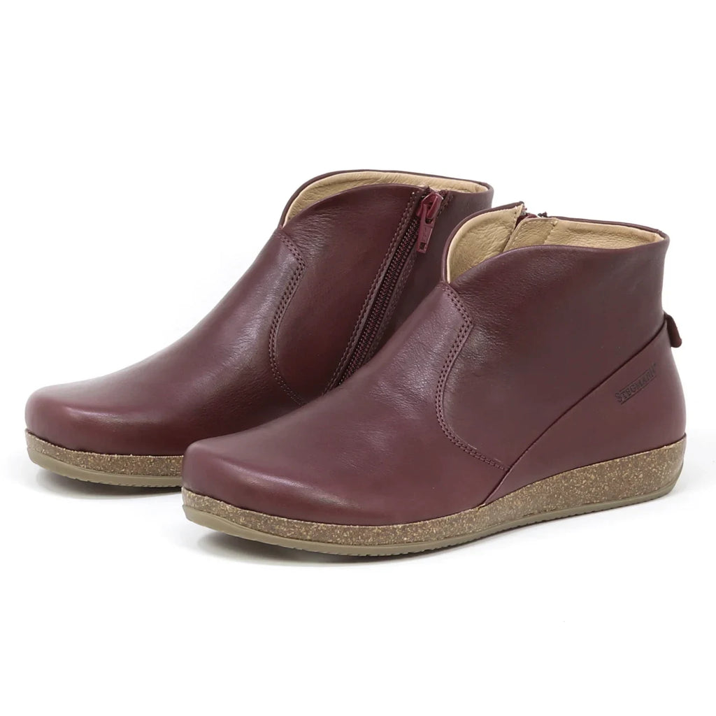 The Women's Leather Amalia Boot features burgundy leather, side zippers, and tan textured wedge soles, shown on a white background.
