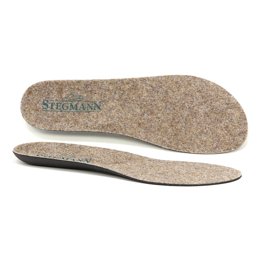 Two brown Women's Wool Contour Replacement Insoles w/Arch are displayed, each featuring a black underside—one laid flat to showcase the visible Stegmann logo, and the other angled to highlight its thickness and built-in arch support. These premium insoles are crafted to deliver superior comfort and enhanced support for all-day wear.