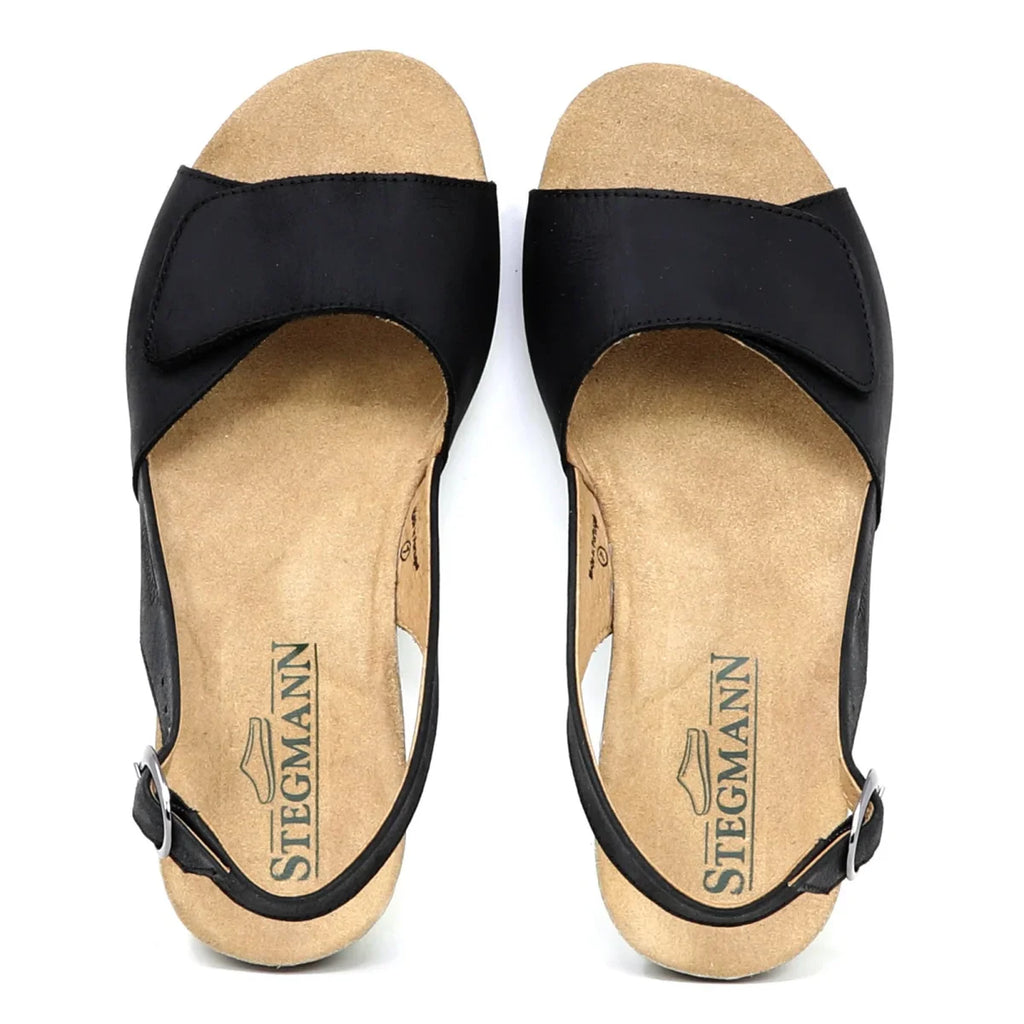 The Women's Clara Slingback Sandal features black open-toe design with ankle straps, a beige sole, and branded Stegmann insoles. These supportive sandals also offer a cushioned footbed for added comfort and are displayed flat on a white background.