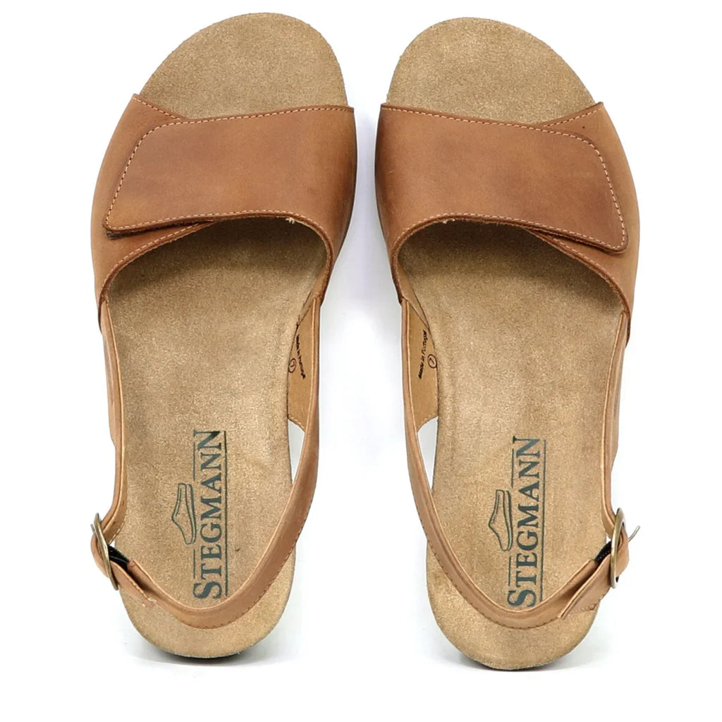 The Women's Clara Slingback Sandal features brown leather with flat soles, an open-toe design, and an adjustable buckle strap. Its Stegmann cushioned footbed ensures enhanced comfort, ideal for all-day wear.