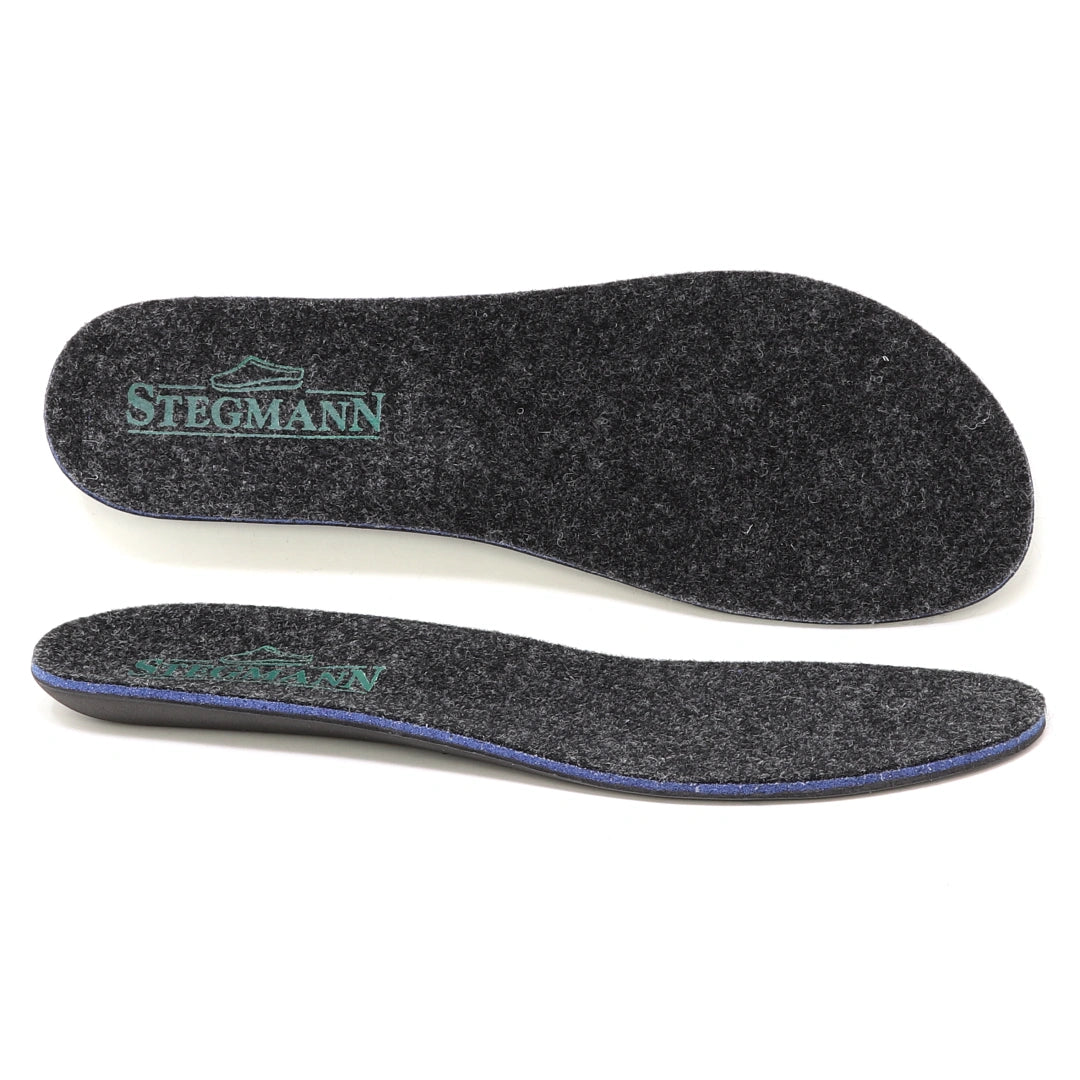 Two dark gray Women’s Wool Contour Plus+ Replacement Insoles w/Arch, featuring “Stegmann” and a shoe logo printed in green on the heel area, are shown from both top and side views. These insoles are designed with arch support for enhanced comfort throughout your day.