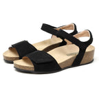 A pair of Women's Freya Leather Wedge Sandals in black with cork soles and Velcro straps, featuring recycled rubber traction outsoles for enhanced grip, viewed at an angle.