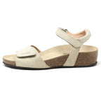 The Women's Freya Leather Wedge Sandal, shown in beige from the side, has a cork sole, adjustable ankle strap, and recycled rubber traction outsole.