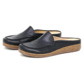 A pair of Women's Greta Leather Mule slip-on shoes in black leather with cork soles and tan interiors, designed for enhanced arch support, displayed on a white background.