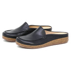 A pair of Women's Greta Leather Mule slip-on shoes in black leather with cork soles and tan interiors, designed for enhanced arch support, displayed on a white background.