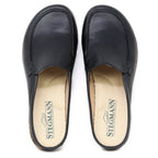 A pair of Women's Greta Leather Mule slip-on shoes in black leather, offering arch support and featuring beige insoles with the Stegmann logo and a shoe graphic.