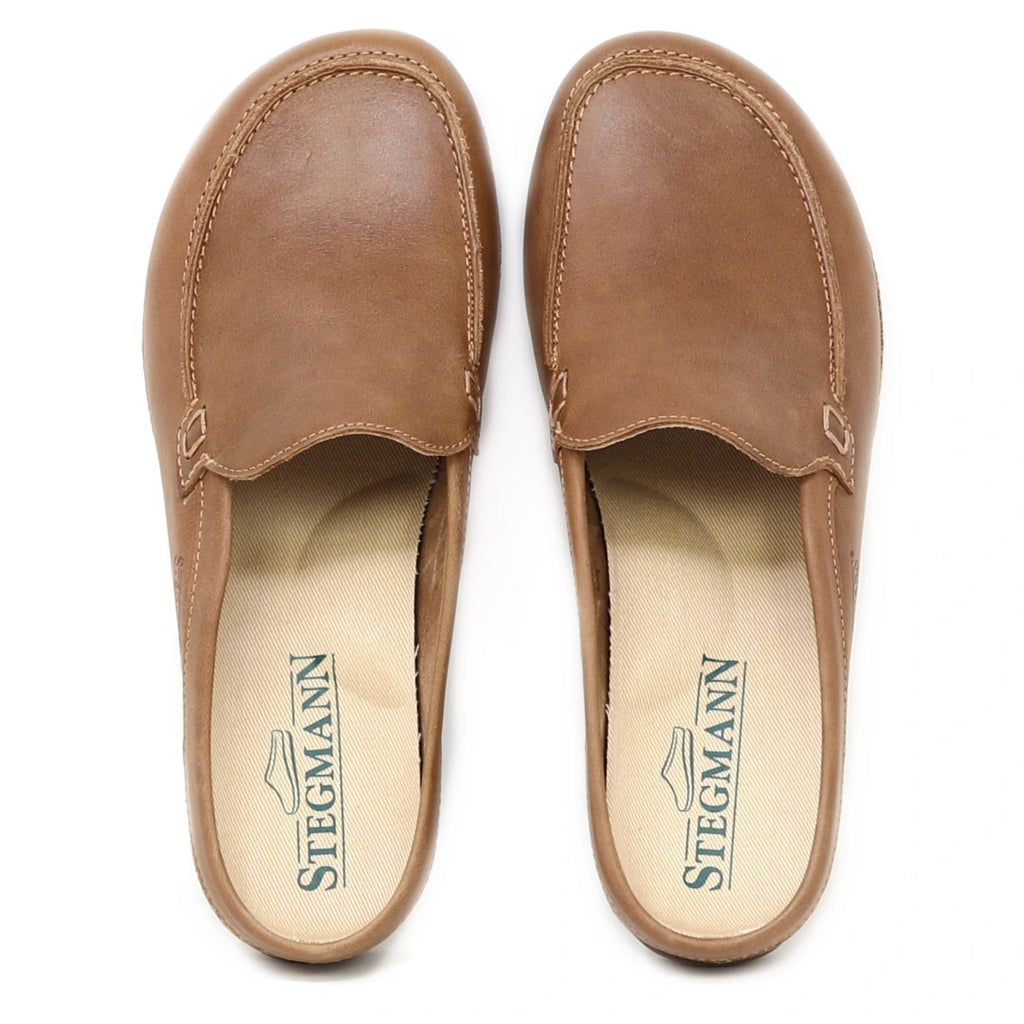A pair of Women's Greta Leather Mule slip-on shoes in brown leather, featuring beige insoles with the Stegmann logo printed in green and providing excellent arch support.