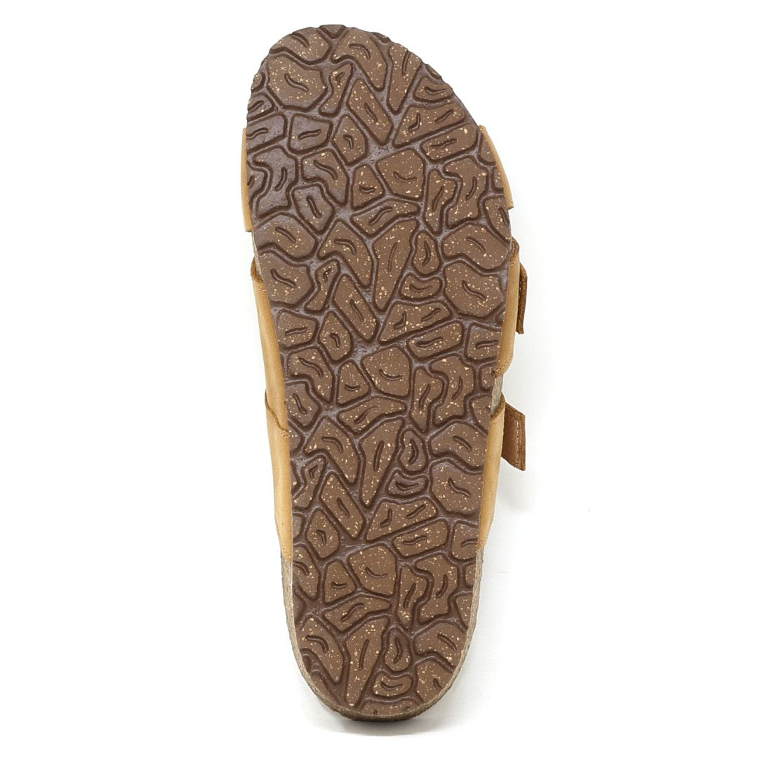 The image features the patterned sole of a brown Women's Hannah Leather Sandal - Medium seen from below, highlighting its textured, abstract design. This sandal provides comfort with arch support and a cushioned suede footbed.