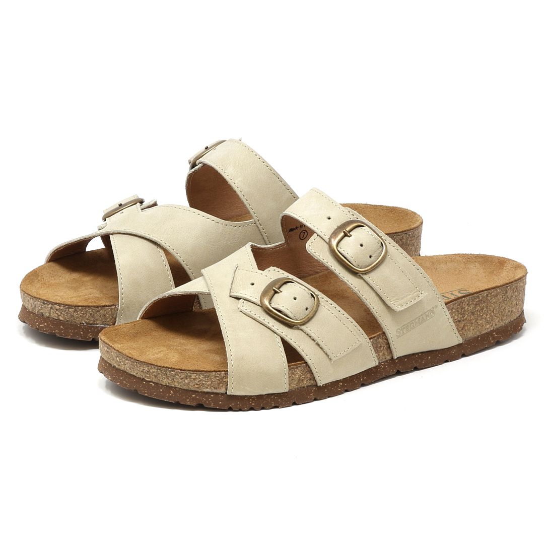 A pair of Women's Heidi Leather Sandals in beige, featuring cork soles, ultra-cushy footbeds, and two adjustable buckle straps on each shoe.