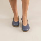 A person wearing Women's Helene Stretch Leather Ballet Flats stands on a light beige floor.