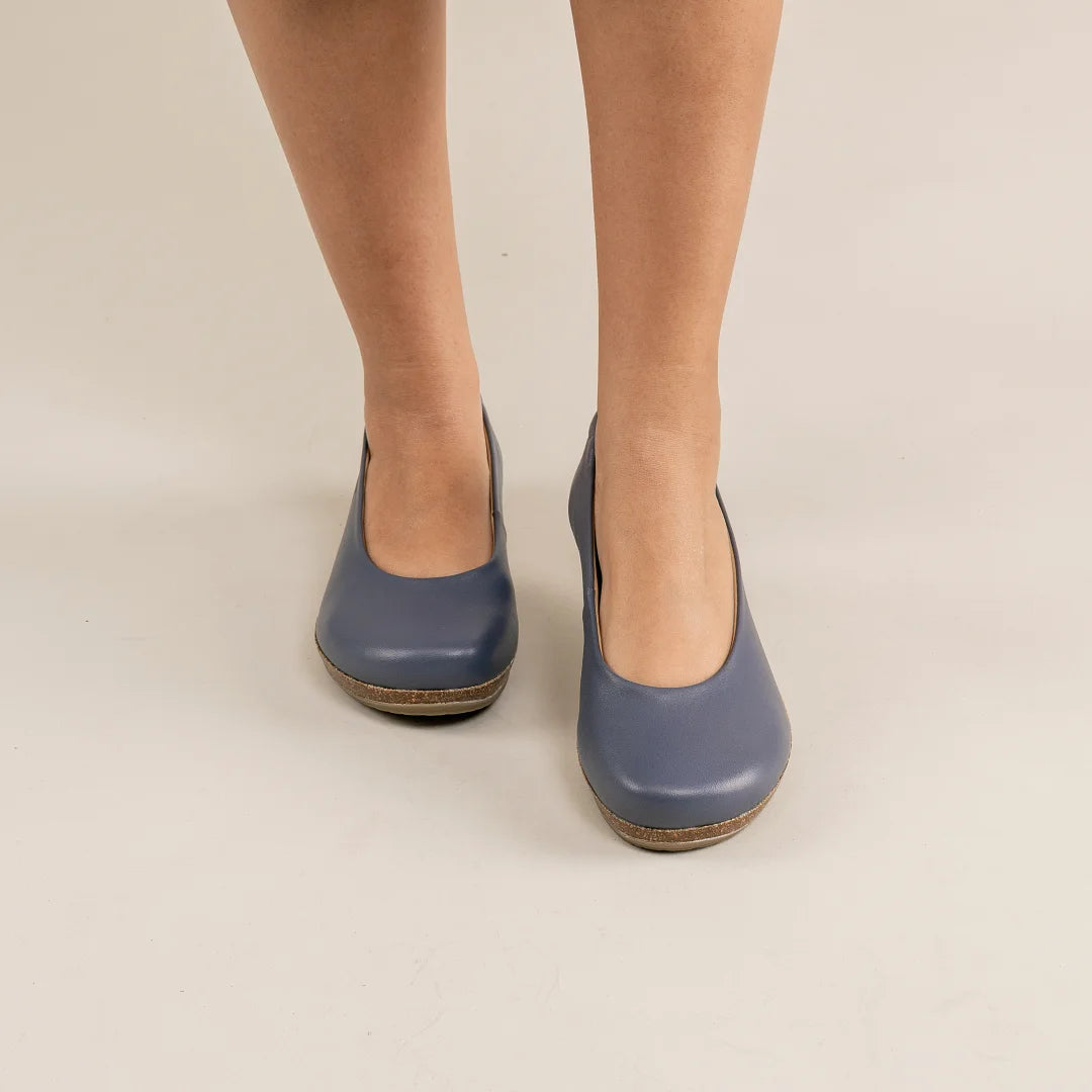 A person wearing Women's Helene Stretch Leather Ballet Flats stands on a light beige floor.