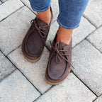Women's Mainz Leather Moc Shoes with laces pair perfectly with blue jeans, gracing a stone-tiled pavement.