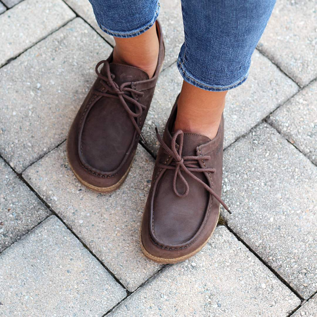 Women's Mainz Leather Moc Shoes with laces pair perfectly with blue jeans, gracing a stone-tiled pavement.