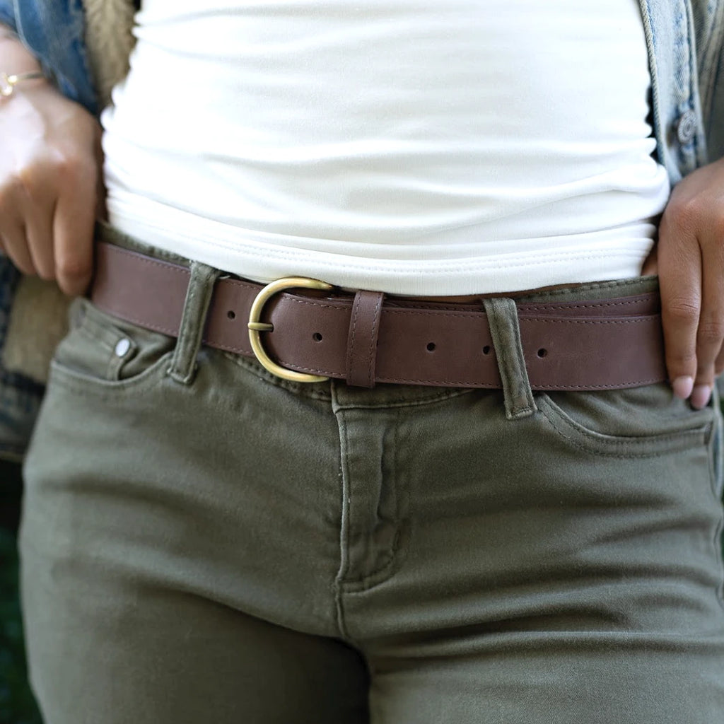 Person wearing olive green pants, a Women’s Matching Leather Belt with a gold buckle, and a white shirt, hands resting on waistband.