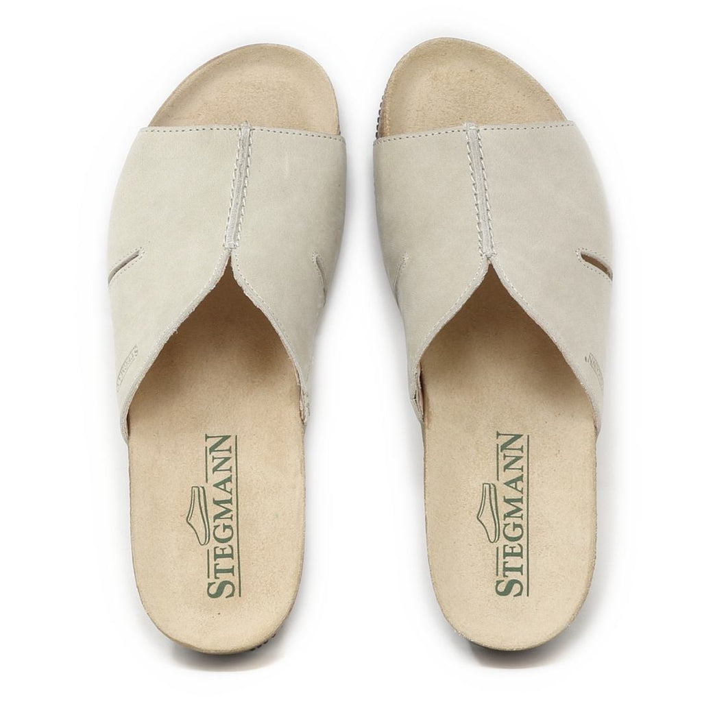 The Women's Layna Leather Wedge Sandal is a pair of light beige open-toe leather slip-on sandals with a sustainable cork midsole and "Stegmann" inscribed on the cushioned suede footbeds.