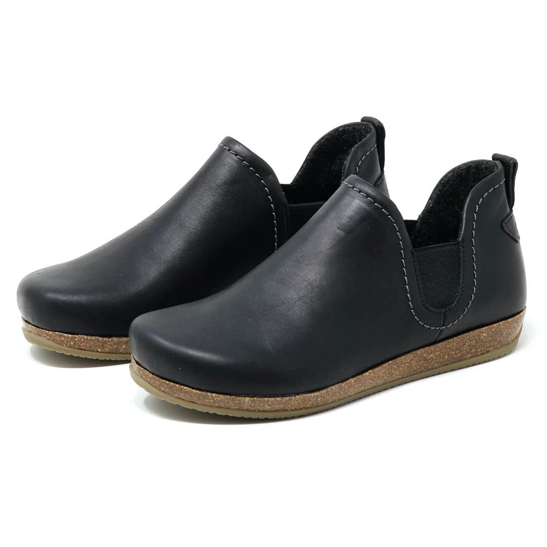 The Women's Lieben Leather Chelsea Boot is a black slip-on with closed toes, elastic side panels, brown textured soles, and a cozy wool felt lining, shown on a white background.
