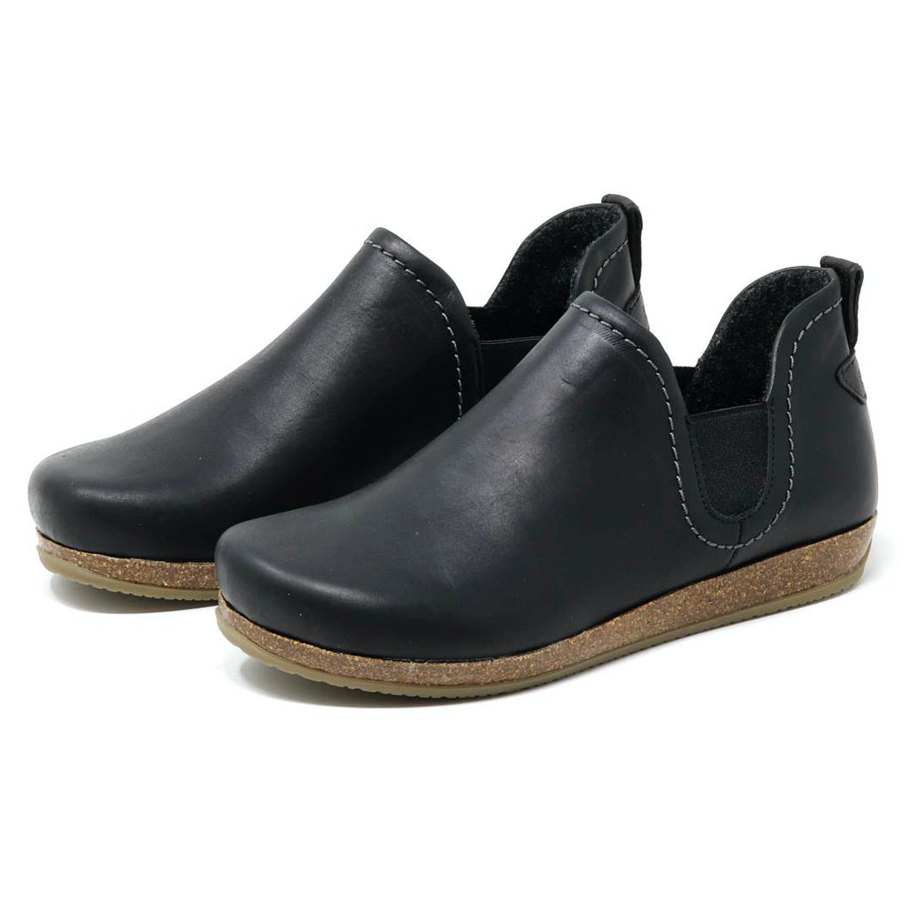 The Women's Lieben Leather Chelsea Boot is a black slip-on with closed toes, elastic side panels, brown textured soles, and a cozy wool felt lining, shown on a white background.