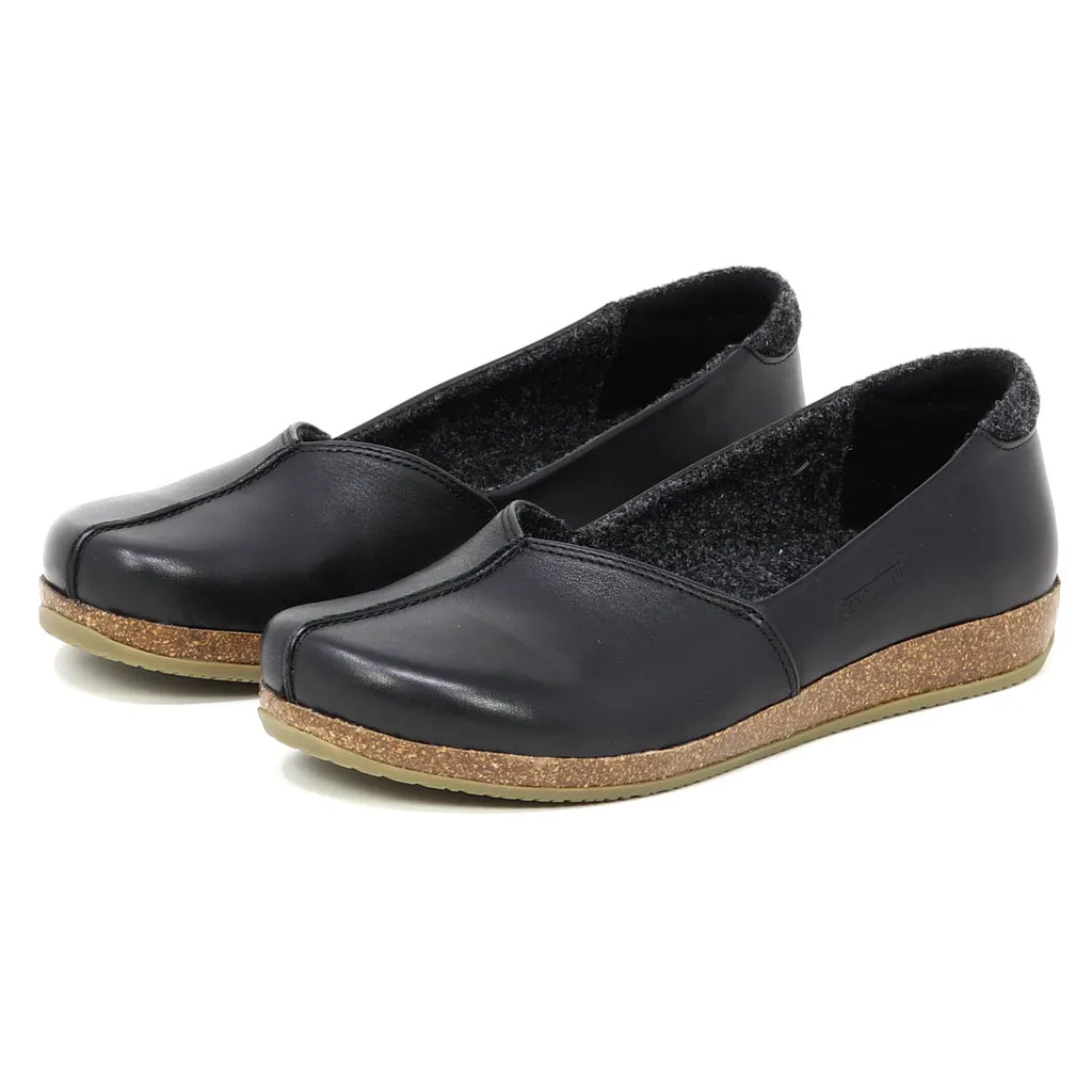 The Women's Liesl Leather Skimmer is a pair of black leather slip-on shoes featuring an anatomically shaped support sole with brown cork and low heels, displayed from an angle.