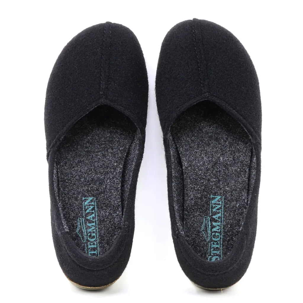 A pair of black Women's Liesl Wool Skimmer slippers with grey insoles, arch support, and "Stegmann" printed in blue on the heel.