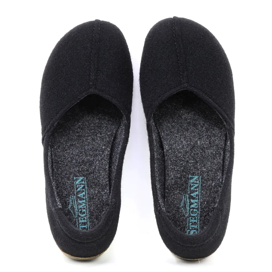 A pair of black Women's Liesl Wool Skimmer slippers with grey insoles, arch support, and "Stegmann" printed in blue on the heel.