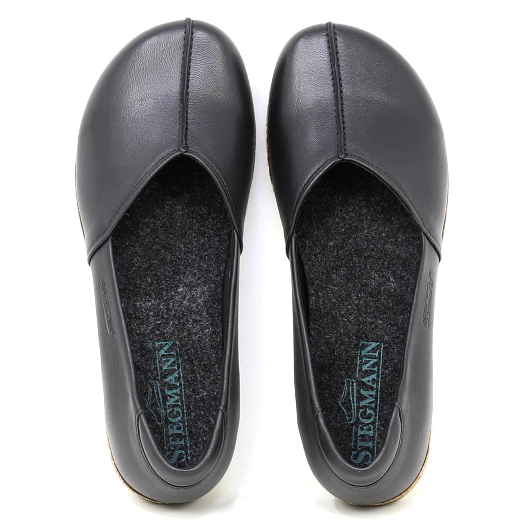 The Women's Liesl Stretch Leather Skimmer is a pair of black slip-on shoes made from buttery-soft leather, featuring a wide toe box, grey felt insoles, and "Stegmann" branding inside each shoe.