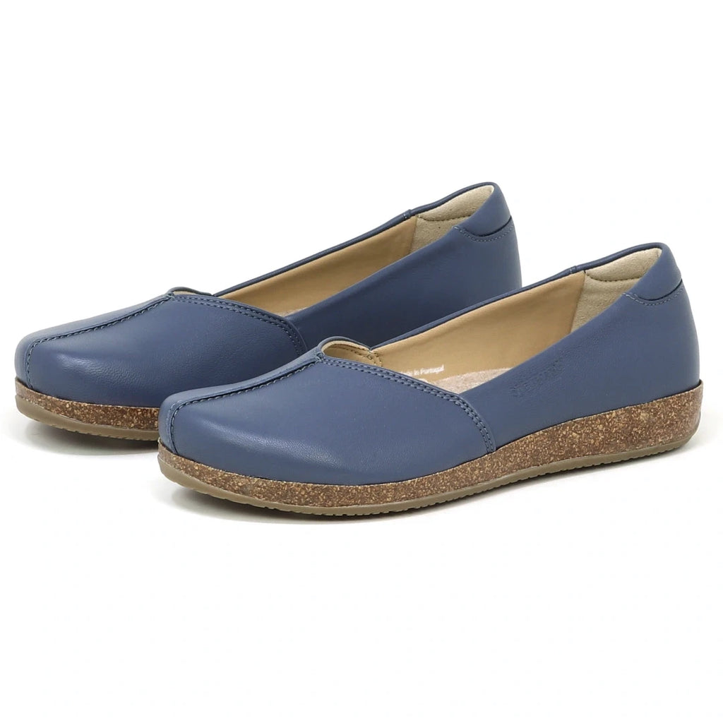 The Women's Liesl Stretch Leather Skimmer is a pair of blue slip-on shoes with rounded toes, wide toe box, cork-textured soles, and buttery-soft leather, displayed against a white background.