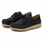 The Women's Mainz Leather Moc Shoe features an oiled black leather upper, cork soles, and black laces. Its sleek design is highlighted against a white background.