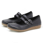 A pair of Women's Marielle Stretch Leather Mary-Jane shoes in black, featuring two buckle straps and cork-textured soles, crafted from stretch leather for added comfort, positioned side by side on a white background.