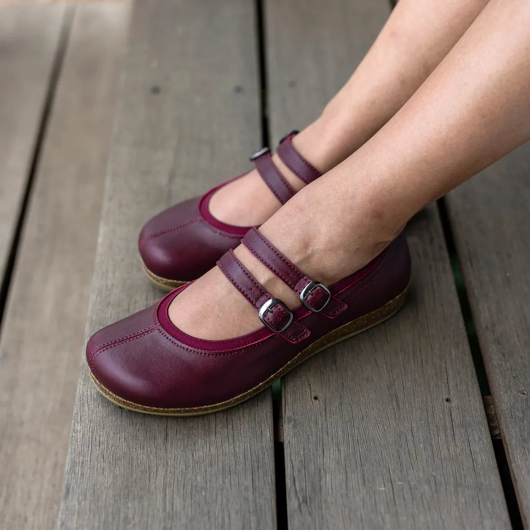 A woman wearing Women's Marielle Stretch Leather Mary-Jane shoes, featuring double straps and arch support, stands on a wooden floor.