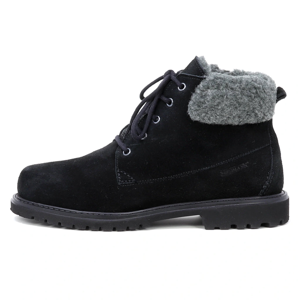 The Women’s Merano Chukka Boot is a black suede ankle boot with a gray padded collar, black laces, and a rugged rubber sole, shown in side profile on a white background. This winter chukka boot features waterproof suede and luxurious wool shearling lining for added warmth and comfort.