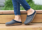 A person wearing blue jeans and the Women's Original 108 Wool Clog - Medium, which features a sleek design and a cork & latex sole, stands on wooden steps outdoors.