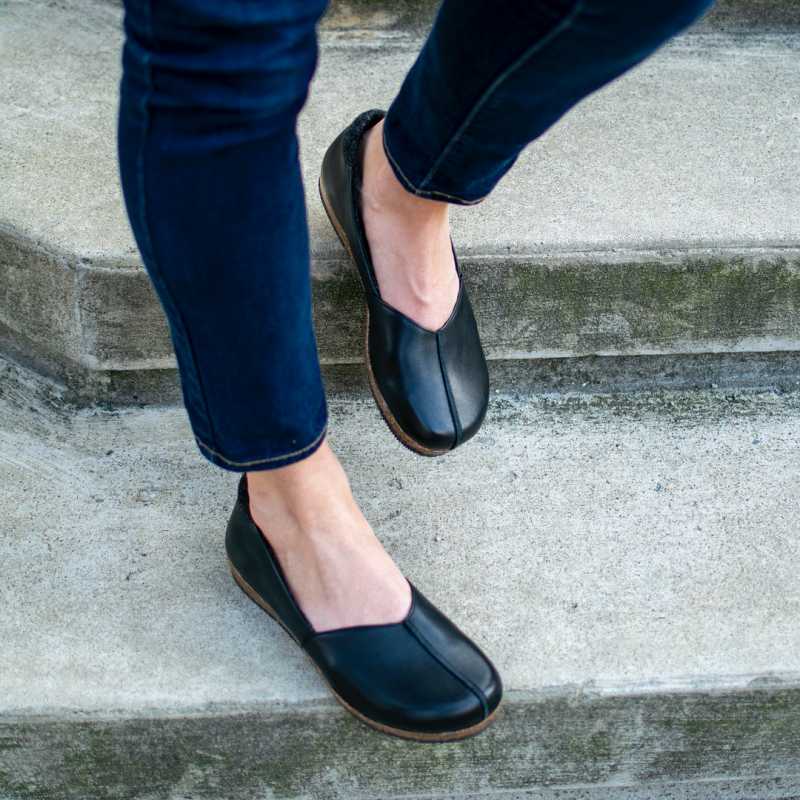 A person wearing dark blue jeans and Women's Liesl Leather Skimmer shoes, which feature a leather upper and wool felt lining, walks down concrete steps.