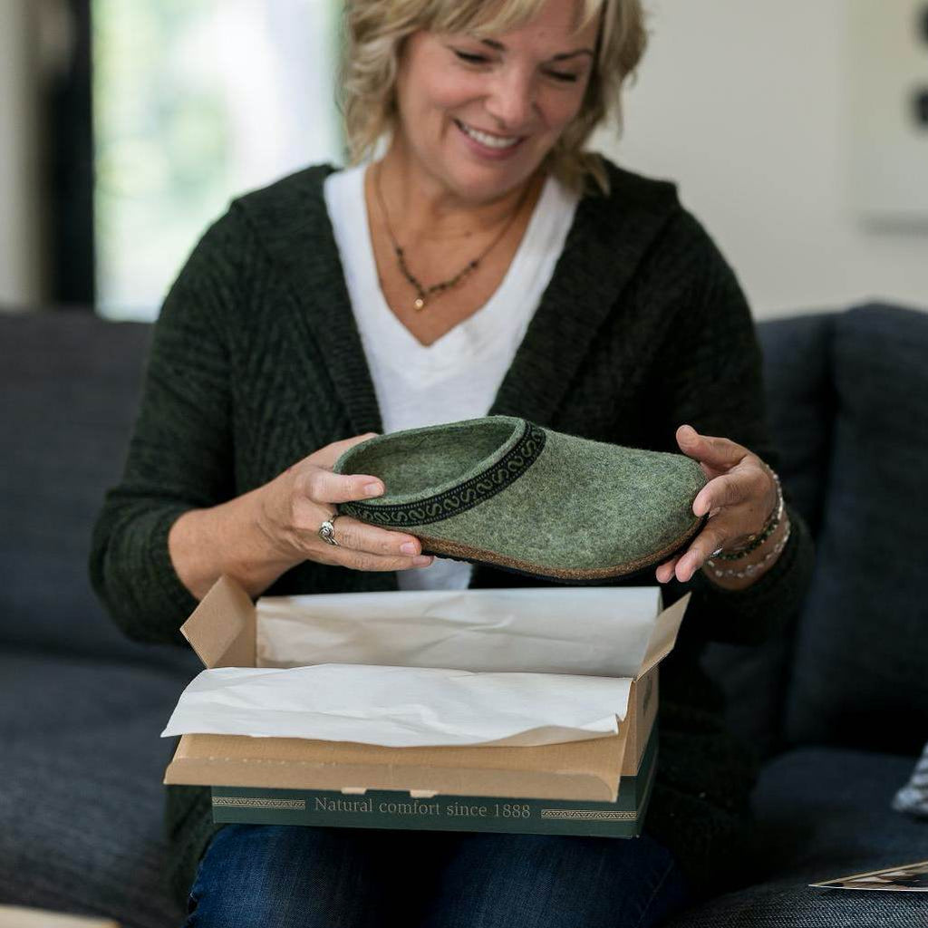 A woman holding the The Original 108 Clog - Sage colorway as she opens the shoe box.