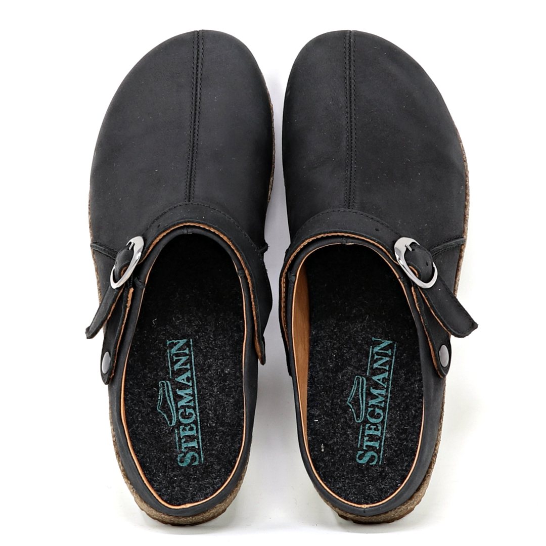 The Women's Tirol Leather Clog features black slip-on clogs with adjustable straps, cork soles, and oiled leather. A wide toe box is complemented by the Stegmann logo on the insole.