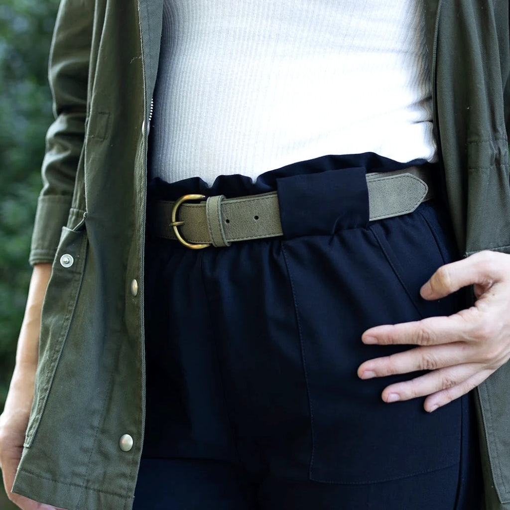 Person wearing a green jacket, white top, and black pants with an elastic waistband and a Women’s Matching Leather Belt, standing outdoors with one hand on their hip.