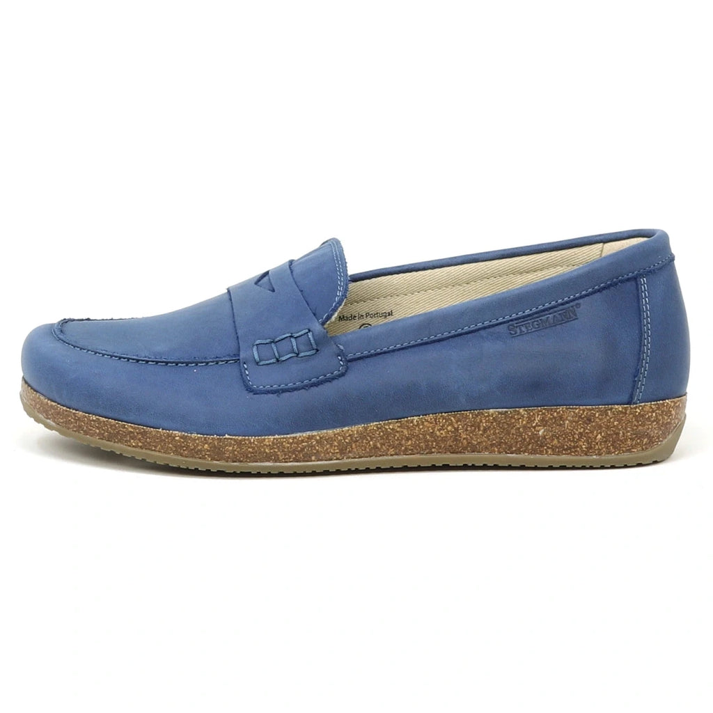 The Women's Victoria Loafer in blue nubuck features visible stitching, a cork-textured sole, cushioned insole, and low heel, shown from the side against a white background.