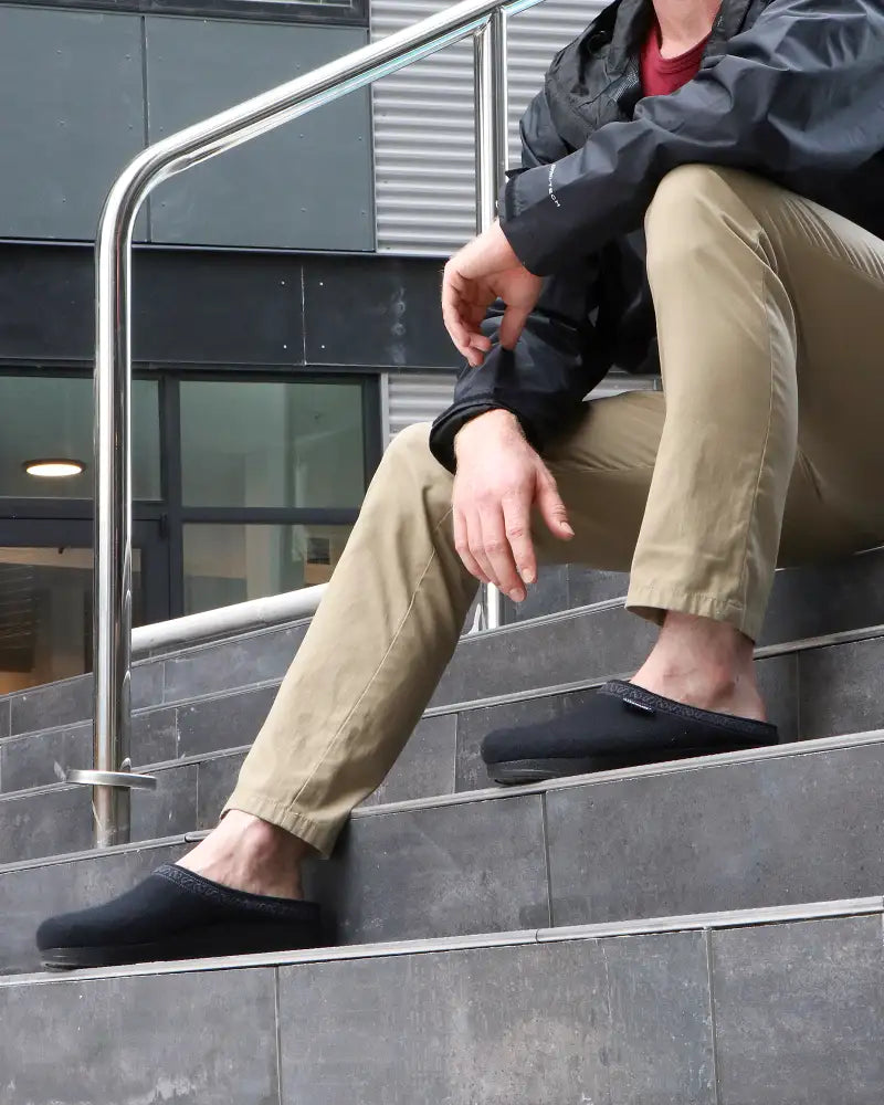 Person sitting on stairs wearing black slippers and beige pants.