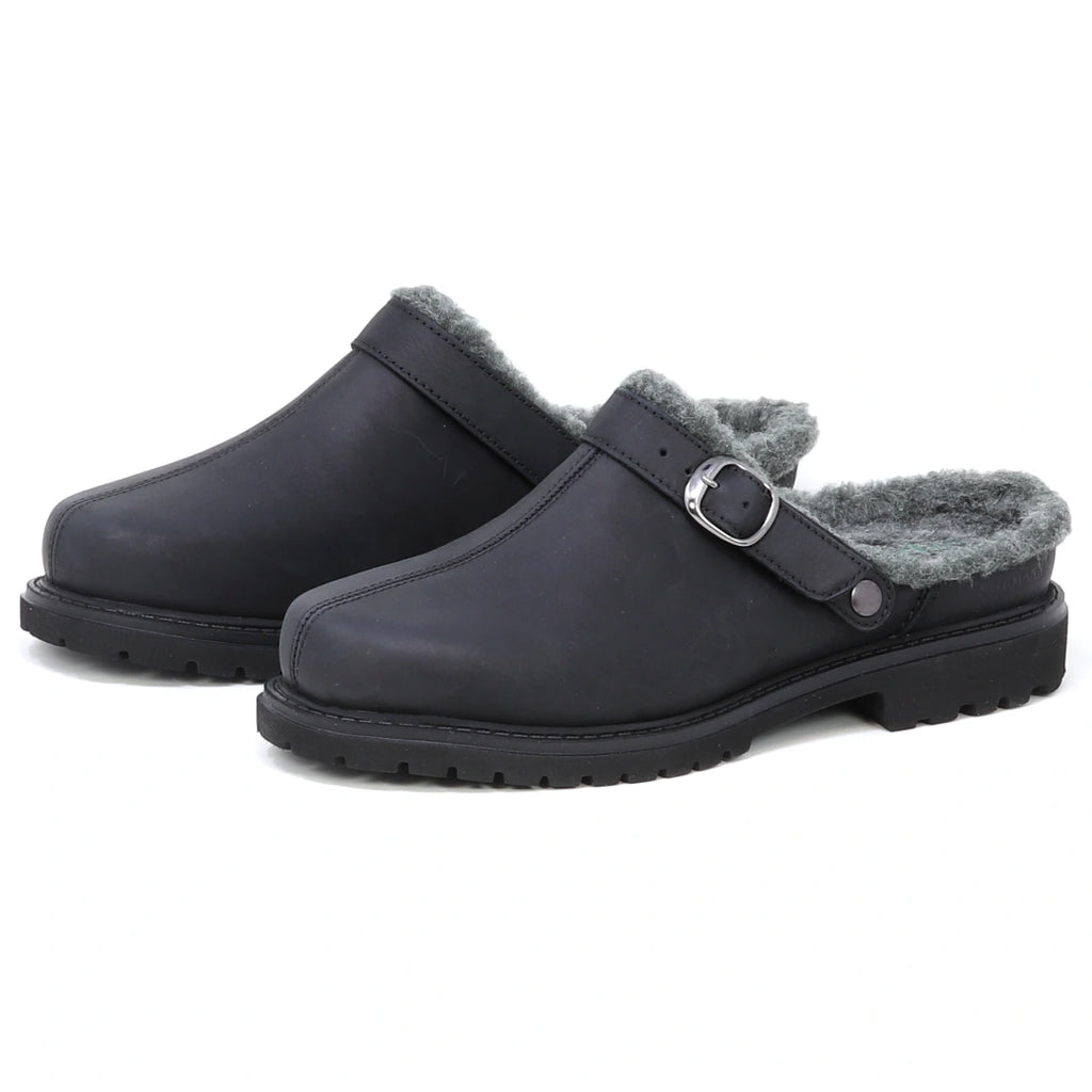 A pair of Zermatt Wool Shearling Clogs in black, designed as backless slip-ons with grey faux fur lining that mimics classic wool shearling, featuring a side buckle strap and rugged rubber soles.