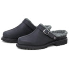 A pair of Zermatt Wool Shearling Clogs in black, designed as backless slip-ons with grey faux fur lining that mimics classic wool shearling, featuring a side buckle strap and rugged rubber soles.