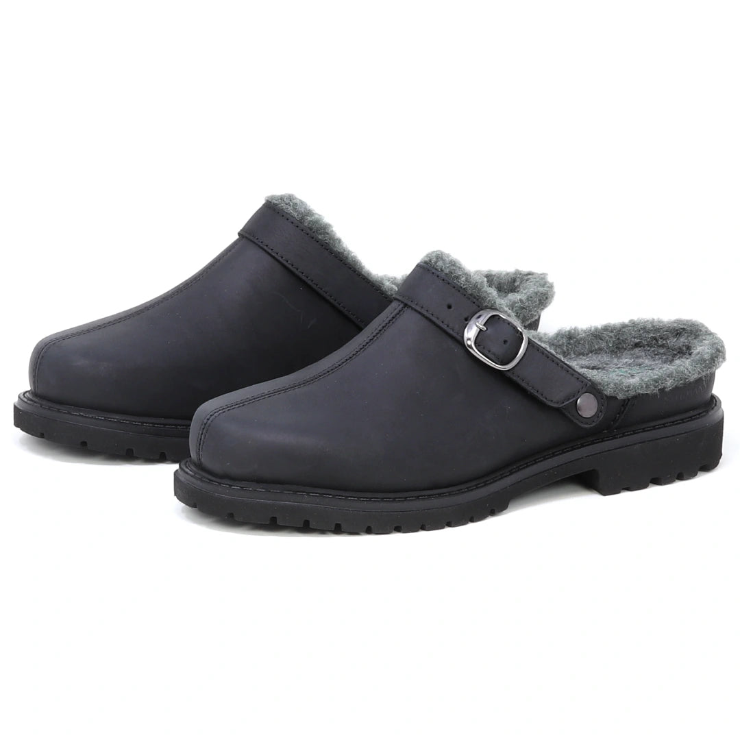 A pair of Zermatt Wool Shearling Clogs in black, designed as backless slip-ons with grey faux fur lining that mimics classic wool shearling, featuring a side buckle strap and rugged rubber soles.