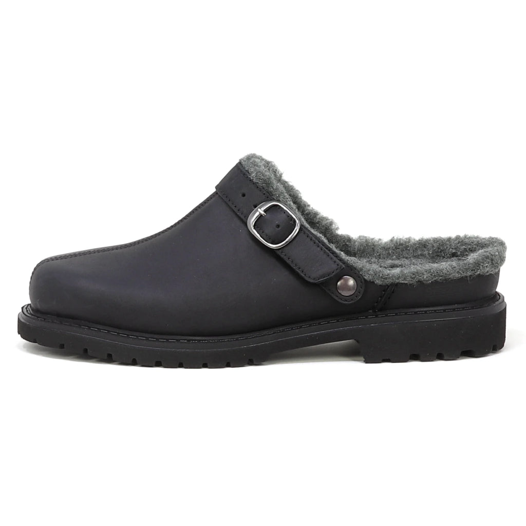 The Zermatt Wool Shearling Clog is a black slip-on clog featuring a buckle strap, cozy wool shearling lining, and a textured rubber sole, displayed in a side profile view against a white background.