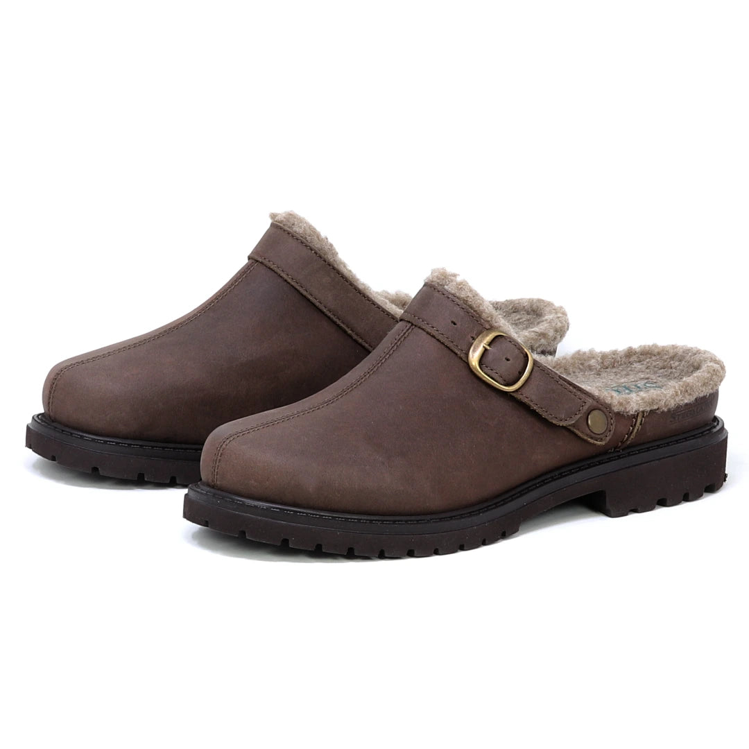 The Zermatt Wool Shearling Clog, featuring brown leather, wool shearling lining, black rubber soles, and brass buckle accents, is displayed on a white background.